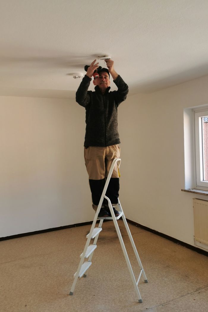 Mastering the First Impression: Your intriguing post title goes here Adult man on ladder fixing a ceiling light in an empty room with beige walls.