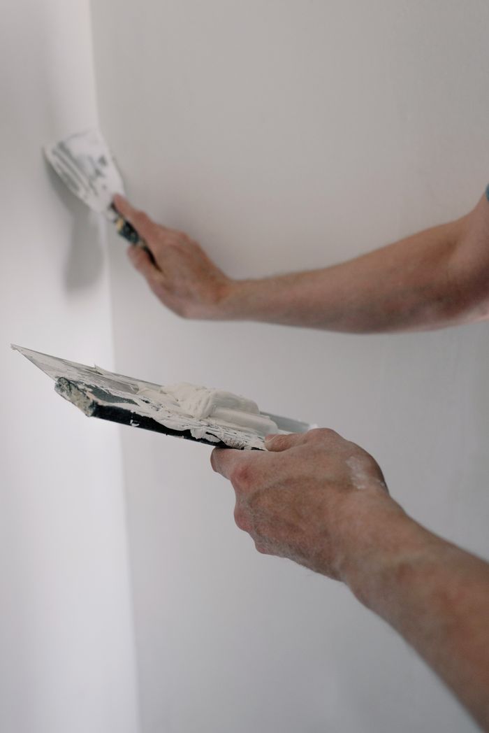 Features Crop male hands holding trowels with putty and renovating walls in room at home