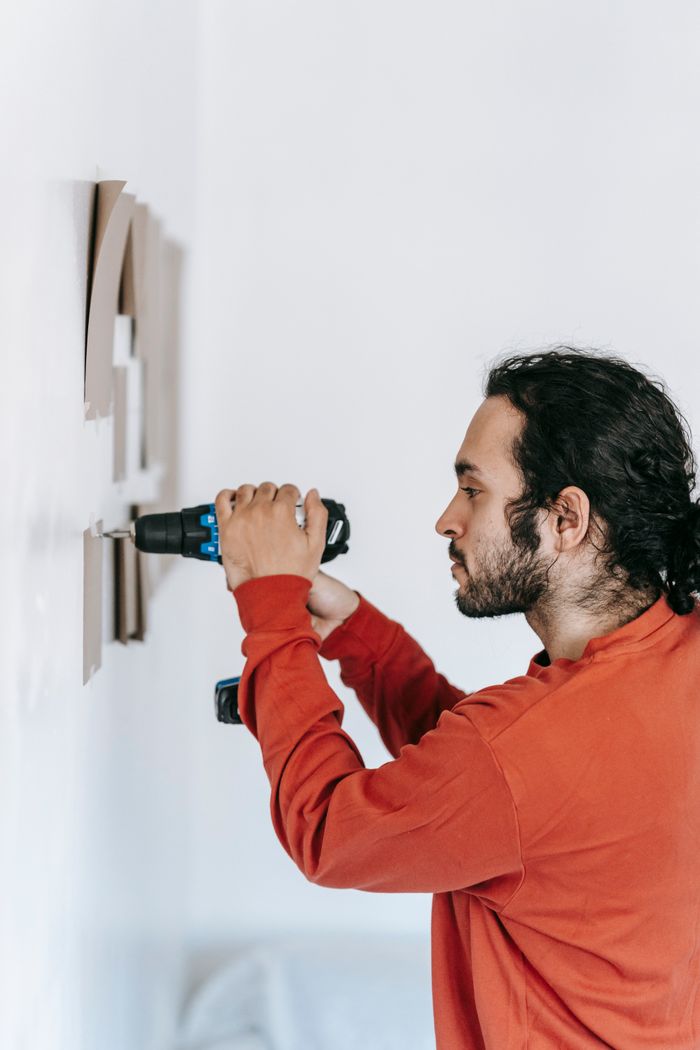 Features Focused man drilling into wall, enhancing home interiors with precision tools.