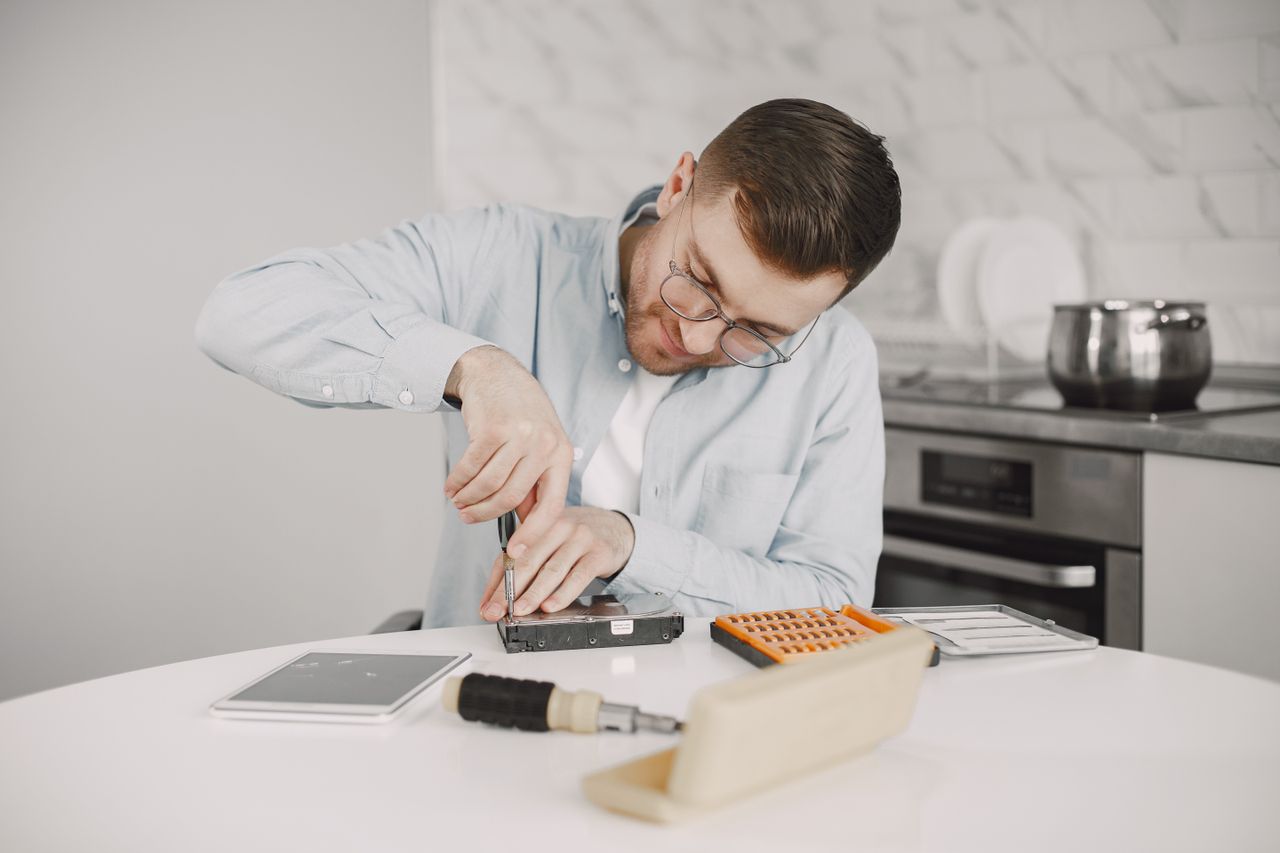 Home Man wearing glasses using a screwdriver to fix a device on a kitchen table.