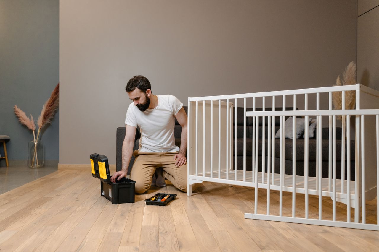 Home A man assembling a white crib indoors with tools, focusing on DIY and home care.
