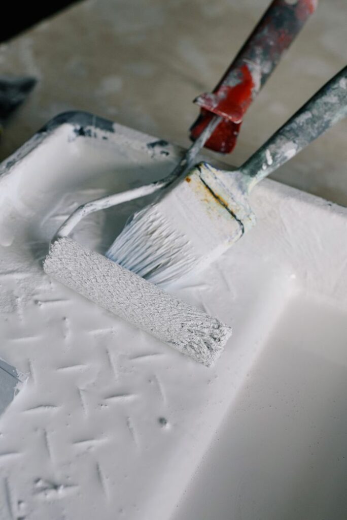 Services High angle wall paint roller and brush placed in paint tray with white pigment in new apartment