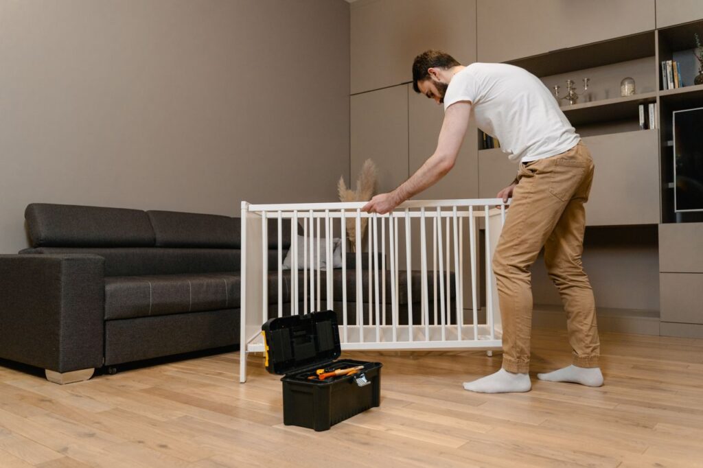 Services A man assembles a crib in a stylish living room with modern decor.